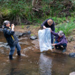 Dawn taking a picture as Sue and Margeret empty a bag of fingerlings into the stream