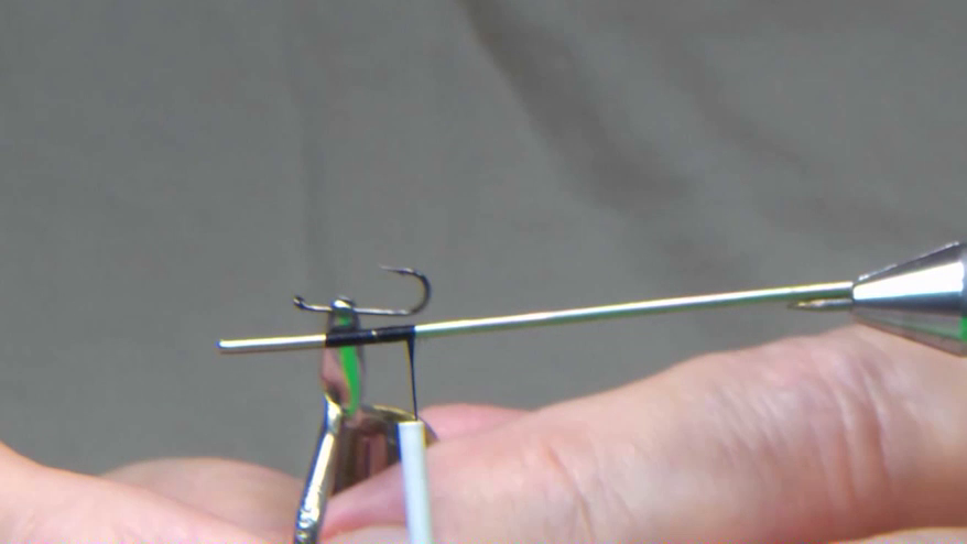 Tying post secured in a vise with thread anchored and wrapped down the post to establish body length, with a hook placed alongside for size comparison and alignment reference.