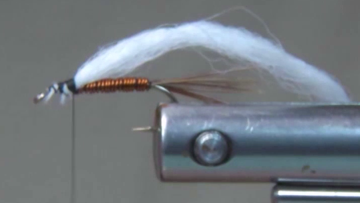 Hook with copper wire body completed and excess trimmed, followed by a smooth black thread base built forward toward the thorax area. A white poly yarn wing is tied in on top of the hook shank, positioned upright to slightly angled to represent an emerger wing profile.